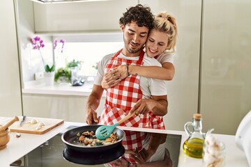 Young couple smiling happy and hugging cooking at kitchen.
