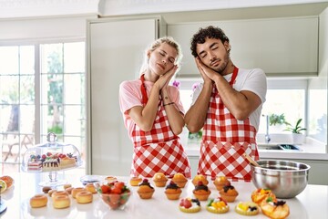 Obraz na płótnie Canvas Couple of wife and husband cooking pastries at the kitchen sleeping tired dreaming and posing with hands together while smiling with closed eyes.