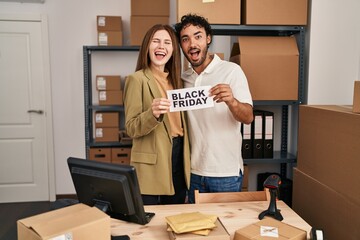 Young two people holding black friday banner at small business store celebrating crazy and amazed for success with open eyes screaming excited.