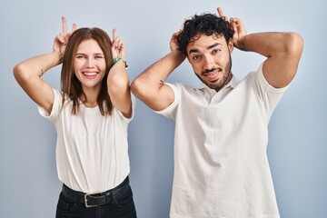 Young couple wearing casual clothes standing together posing funny and crazy with fingers on head...