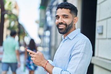 Young arab man smiling confident using smartphone at street