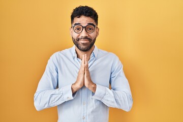 Obraz premium Hispanic man with beard standing over yellow background praying with hands together asking for forgiveness smiling confident.