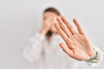 Naklejka premium Young caucasian woman standing over isolated background covering eyes with hands and doing stop gesture with sad and fear expression. embarrassed and negative concept.