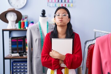 Asian young woman dressmaker standing by manikin puffing cheeks with funny face. mouth inflated with air, catching air.