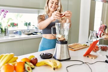 Young woman looking online juice recipe pouring apple on blender at kitchen