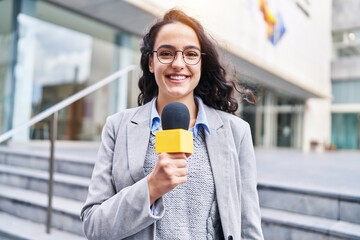 Young hispanic woman reporter working using microphone at street - obrazy, fototapety, plakaty