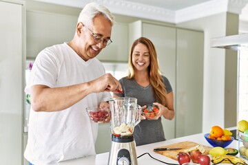 Middle age hispanic couple smiling happy cooking smoothie at the kitchen.