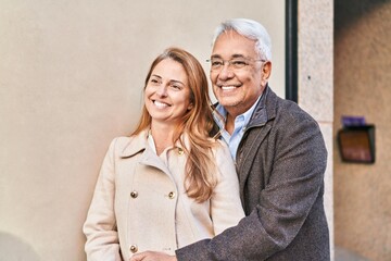Middle age man and woman couple hugging each other standing at street