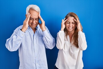 Middle age hispanic couple standing over blue background with hand on head, headache because stress. suffering migraine.
