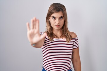 Young hispanic woman standing over isolated background doing stop sing with palm of the hand. warning expression with negative and serious gesture on the face.