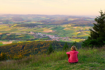 A woman sitting on mount Hohenbogen, looking to Neukirchen Heiligblut, a small town in the Bavarian Forest.