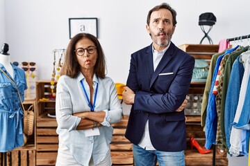 Two hispanic people working as manager at retail boutique making fish face with mouth and squinting eyes, crazy and comical.