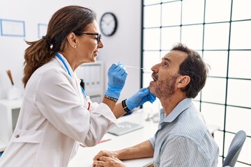 Obraz premium Middle age man and woman wearing doctor uniform making covid-19 test at clinic