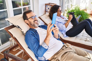 Middle age hispanic couple using touchpad lying on hammock with dog at terrace