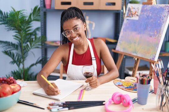 African american woman artist drinking wine drawing on notebook at art studio