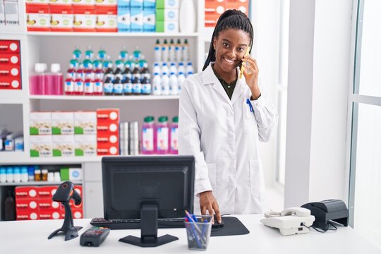 African american woman pharmacist talking on smartphone using computer at pharmacy