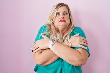 Caucasian plus size woman standing over pink background shaking and freezing for winter cold with...
