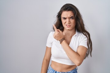 Young teenager girl standing over white background pointing aside worried and nervous with forefinger, concerned and surprised expression