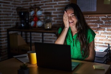 Young teenager girl working at the office at night covering one eye with hand, confident smile on face and surprise emotion.