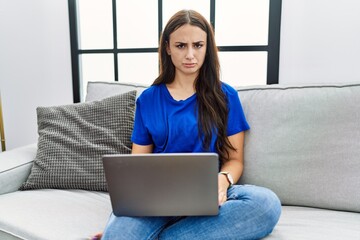 Fototapeta na wymiar Young brunette woman using laptop at home skeptic and nervous, frowning upset because of problem. negative person.
