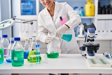 Middle age woman wearing scientist uniform pouring liquid at laboratory