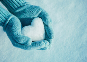 Female hands in knitted mittens with heart of snow in winter day. Love concept. Valentine day background.	
