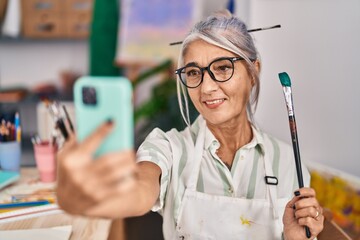 Middle age grey-haired woman artist smiling confident make selfie by smartphone at art studio