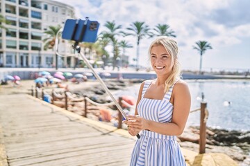 Fototapeta na wymiar Young blonde girl smiling happy making selfie by the smartphone at the beach.