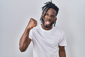 Fototapeta premium African man with dreadlocks wearing casual t shirt over white background angry and mad raising fist frustrated and furious while shouting with anger. rage and aggressive concept.