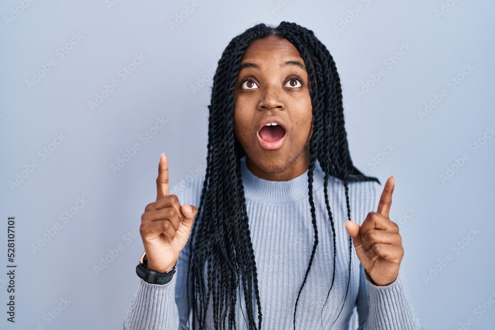 Sticker african american woman standing over blue background amazed and surprised looking up and pointing wi