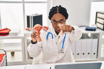 African american doctor woman holding anatomical model of female genital organ pointing with finger to the camera and to you, confident gesture looking serious