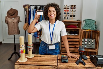 Young latin shopkeeper woman smiling happy holding credit card at clothing store.