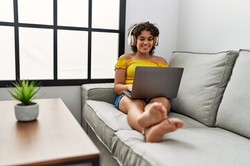 Young hispanic woman smiling confident using laptop and headphones at home