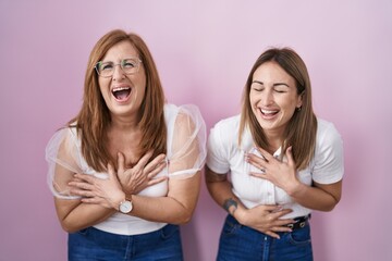 Hispanic mother and daughter wearing casual white t shirt over pink background smiling and laughing hard out loud because funny crazy joke with hands on body.