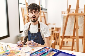 Hispanic man with beard at art studio afraid and shocked with surprise expression, fear and excited...