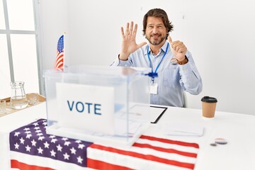 Handsome middle age man sitting at voting stand showing and pointing up with fingers number six while smiling confident and happy.