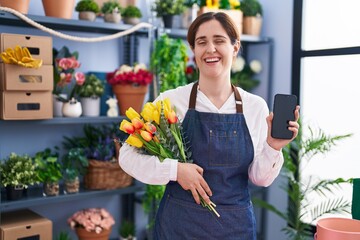 Brunette woman working at florist shop holding smartphone winking looking at the camera with sexy...