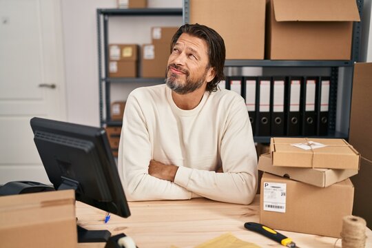 Handsome middle age man working at small business ecommerce smiling looking to the side and staring away thinking.