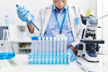 Middle age grey-haired man wearing scientist uniform using pipette at laboratory