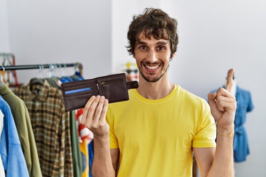 Young hispanic man holding leather wallet at retail shop smiling happy pointing with hand and finger to the side