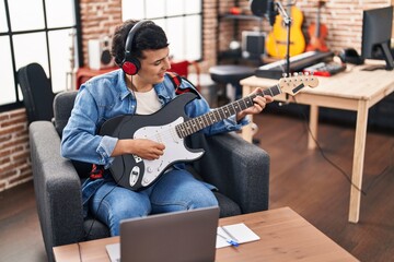 Young non binary man musician having online electric guitar lesson at music studio