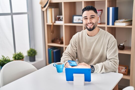 Young arab man using smartphone sitting on table at home