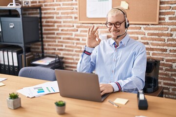 Young caucasian man wearing call center agent headset doing ok sign with fingers, smiling friendly gesturing excellent symbol