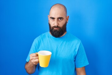 Young hispanic man with beard and tattoos drinking a cup of coffee skeptic and nervous, frowning upset because of problem. negative person.