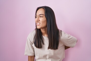 Young hispanic woman standing over pink background suffering of backache, touching back with hand, muscular pain