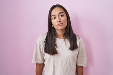 Young hispanic woman standing over pink background looking sleepy and tired, exhausted for fatigue and hangover, lazy eyes in the morning.