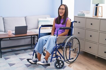 Young hispanic woman sitting on wheelchair at home winking looking at the camera with sexy...