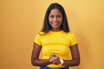 Obraz premium Young indian woman standing over yellow background with hands together and crossed fingers smiling relaxed and cheerful. success and optimistic
