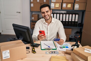Young hispanic man e-commerce business worker using smartphone and credit card at office