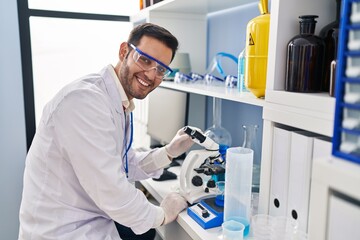 Young hispanic man scientist using microscope at laboratory